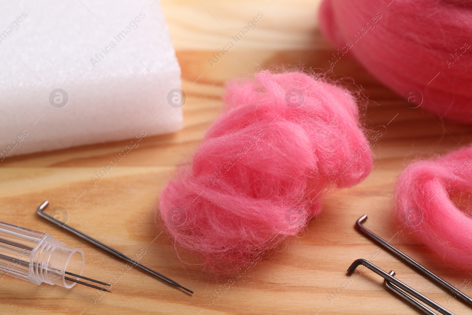 Photo of Pink felting wool and needles on wooden table, closeup