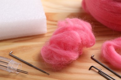 Photo of Pink felting wool and needles on wooden table, closeup