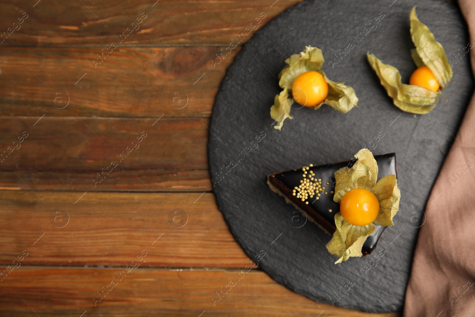 Photo of Piece of tasty cake decorated with physalis fruit on wooden table, top view. Space for text