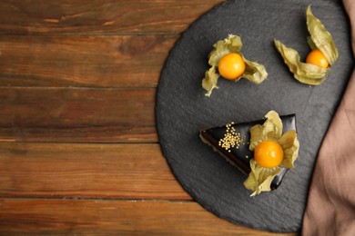 Piece of tasty cake decorated with physalis fruit on wooden table, top view. Space for text