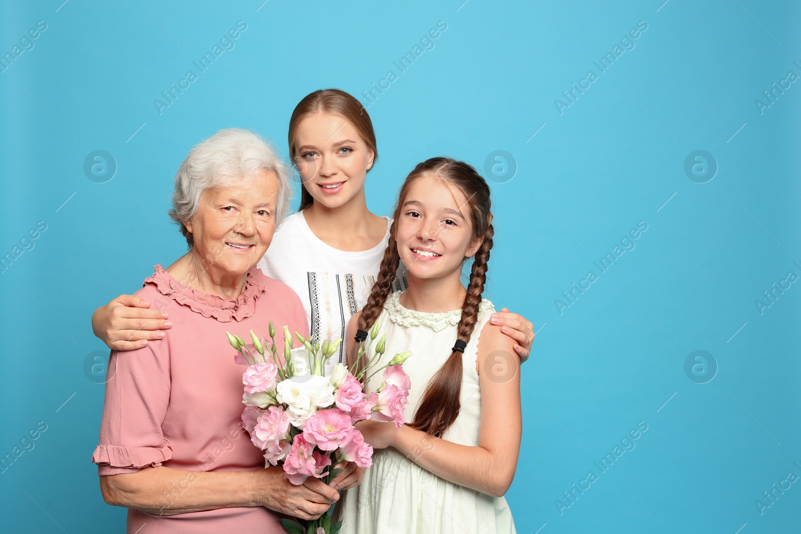 Photo of Happy sisters with their grandmother holding flowers on light blue background
