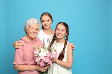 Happy sisters with their grandmother holding flowers on light blue background