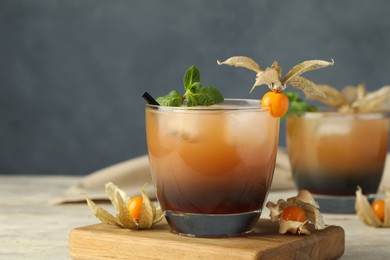 Photo of Refreshing cocktail decorated with physalis fruit on wooden table against grey background
