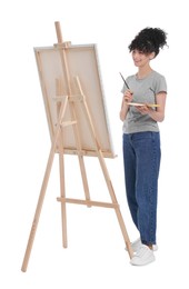 Young woman painting on easel with canvas against white background