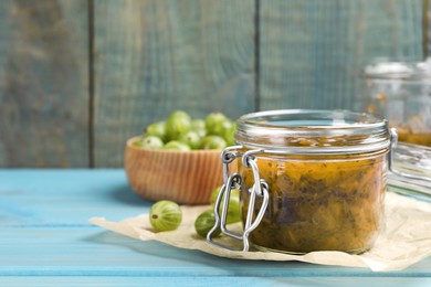 Jar of delicious gooseberry jam and fresh berries on blue wooden table. Space for text
