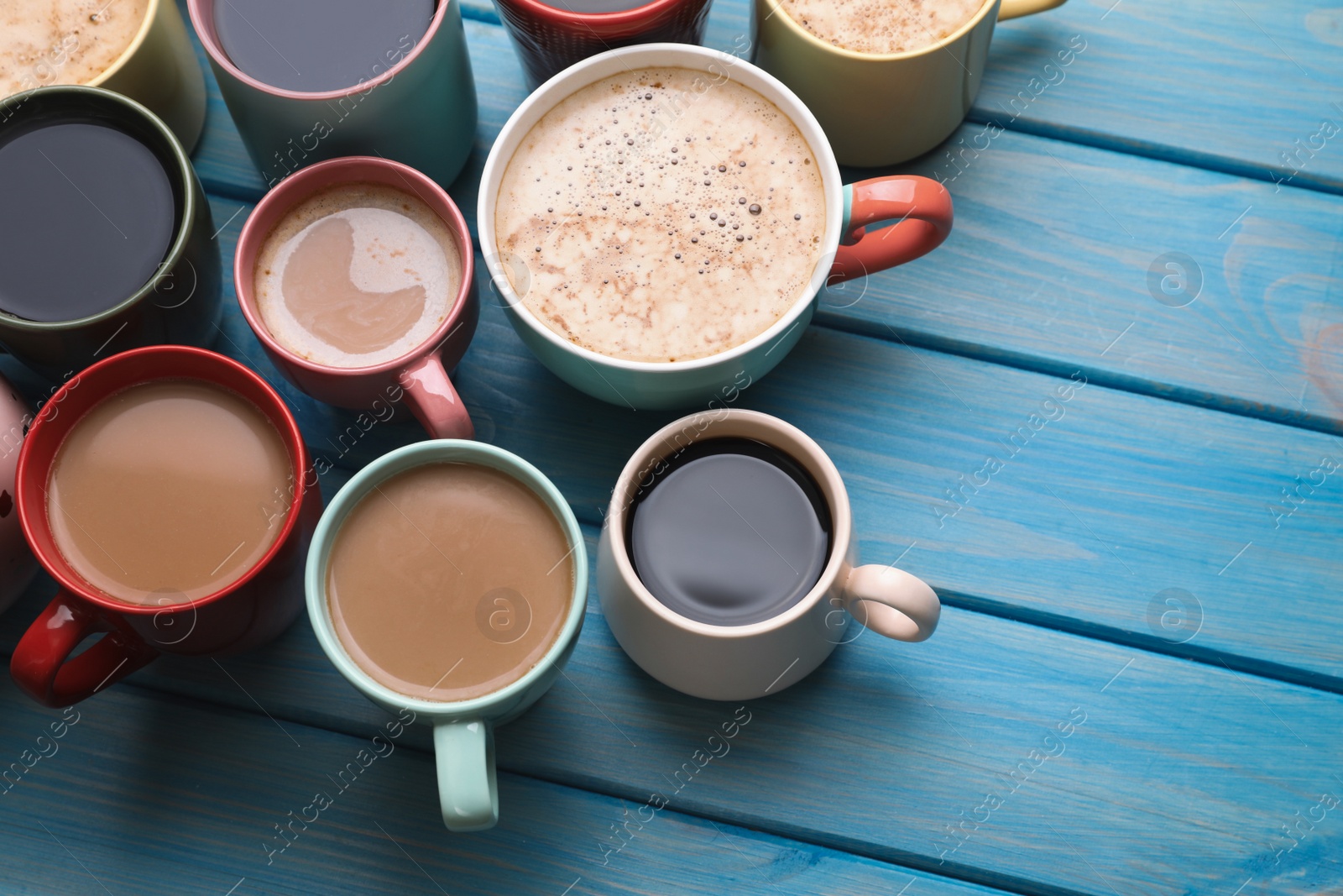 Photo of Many cups of different coffee drinks on light blue wooden table, above view