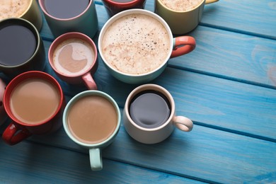 Many cups of different coffee drinks on light blue wooden table, above view