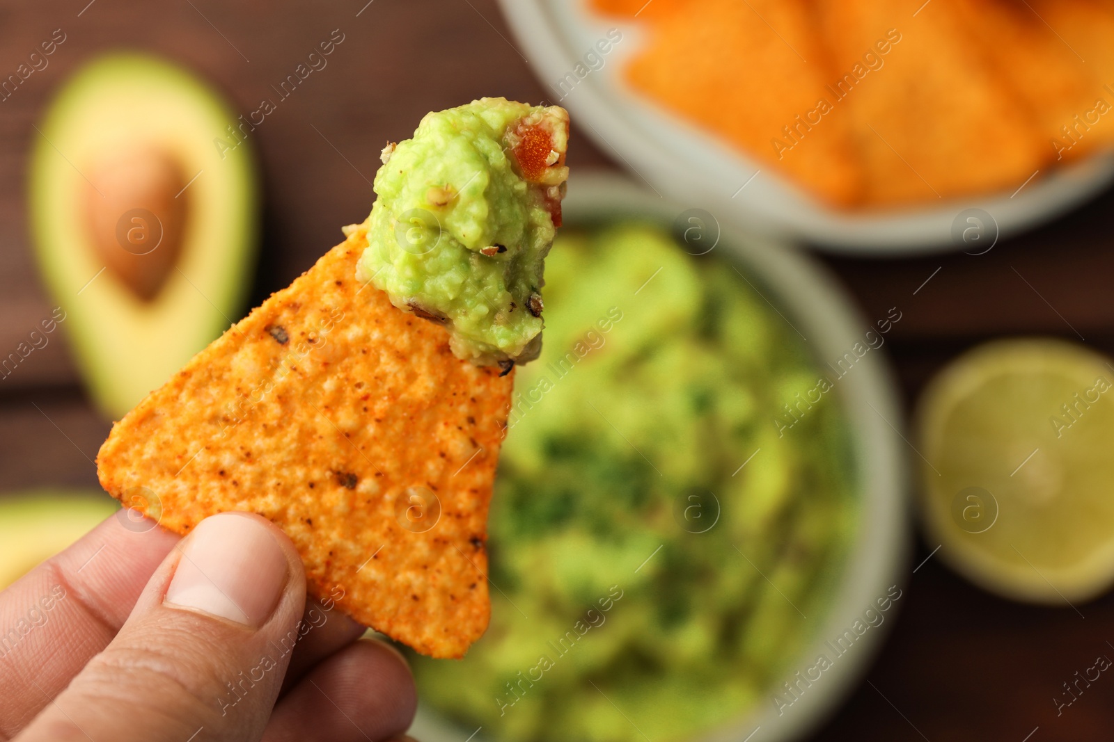 Photo of Woman holding delicious nachos chip with guacamole at table, closeup. Space for text