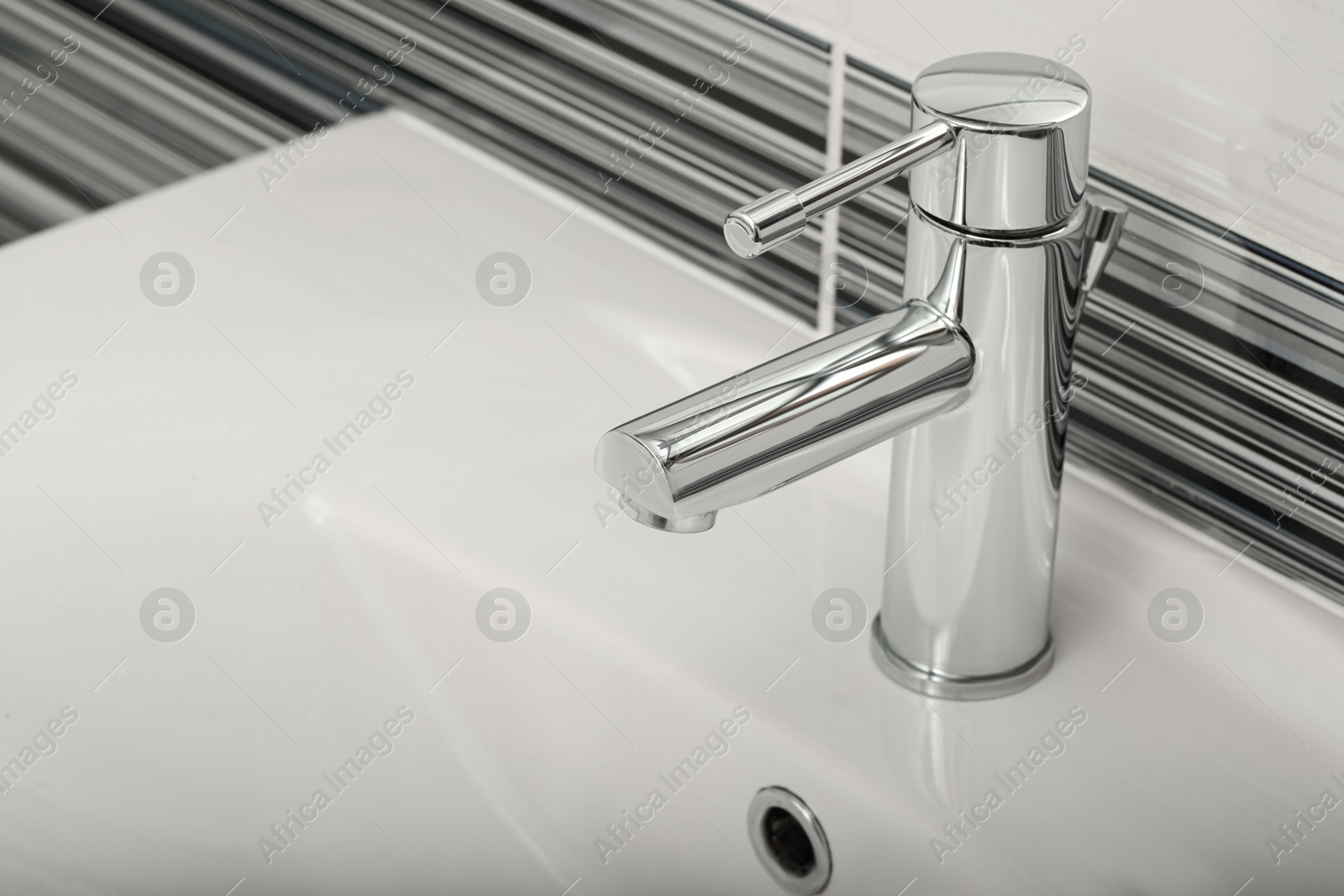 Photo of Clean white sink with shiny water tap in bathroom