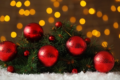 Photo of Fir branches with Christmas balls on snow against blurred festive lights