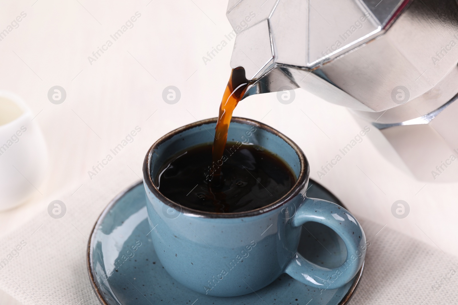 Photo of Pouring aromatic coffee from moka pot into cup at white table, closeup