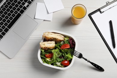 Container of tasty food, laptop, fork and glass of juice on white wooden table, flat lay. Business lunch