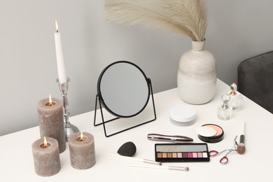 Dressing table with mirror, cosmetic products, perfumes and burning candles in makeup room