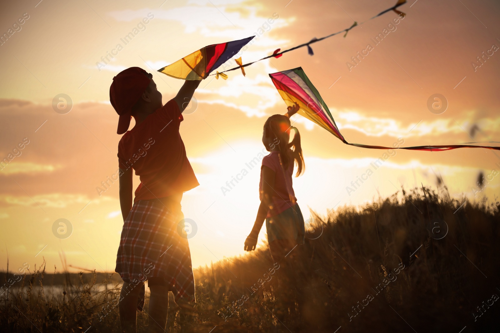 Photo of Little children playing with kites outdoors at sunset. Spending time in nature