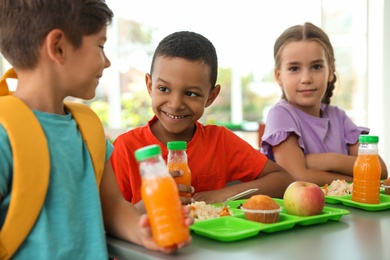 Photo of Children sitting at table and eating healthy food during break at school