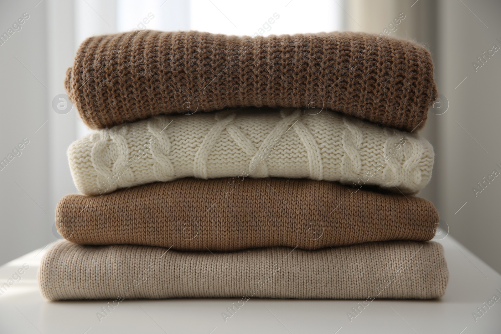 Photo of Stack of folded warm sweaters on white table indoors, closeup