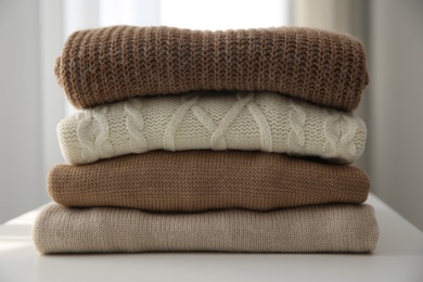 Stack of folded warm sweaters on white table indoors, closeup