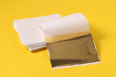 Photo of Edible gold leaf sheets on yellow background, closeup
