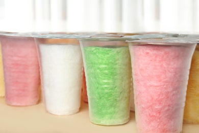 Plastic cups with cotton candy on table against blurred background