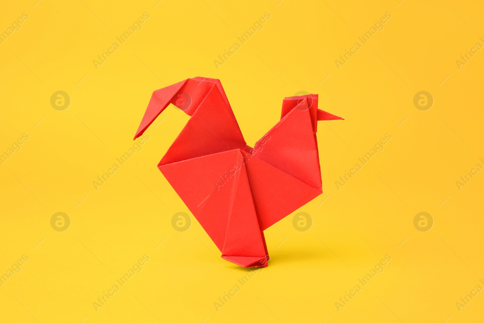 Photo of Origami art. Handmade red paper rooster on yellow background