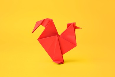 Origami art. Handmade red paper rooster on yellow background