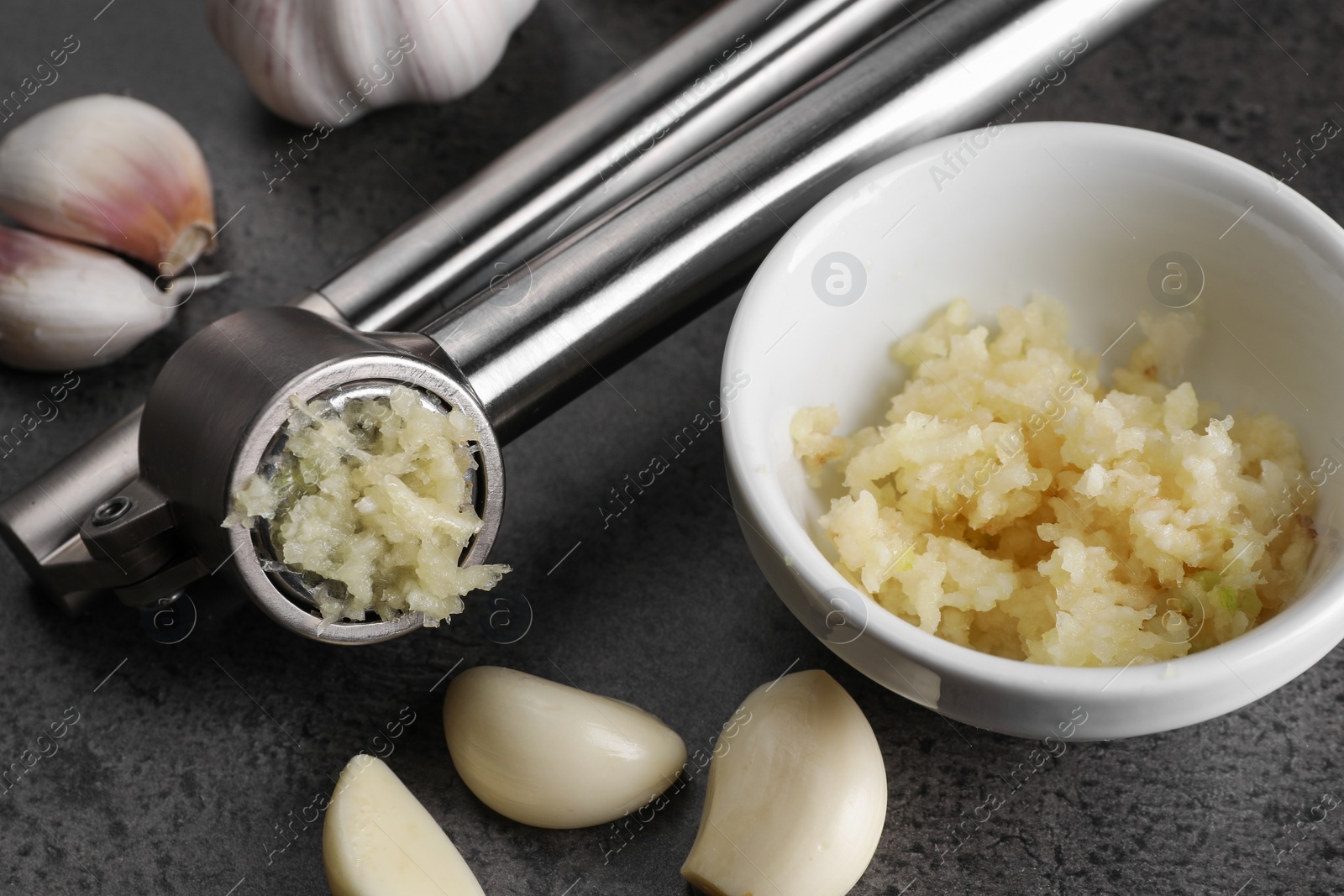 Photo of Garlic press, cloves and mince on grey table, closeup