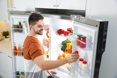 Photo of Young man taking yoghurt out of refrigerator indoors