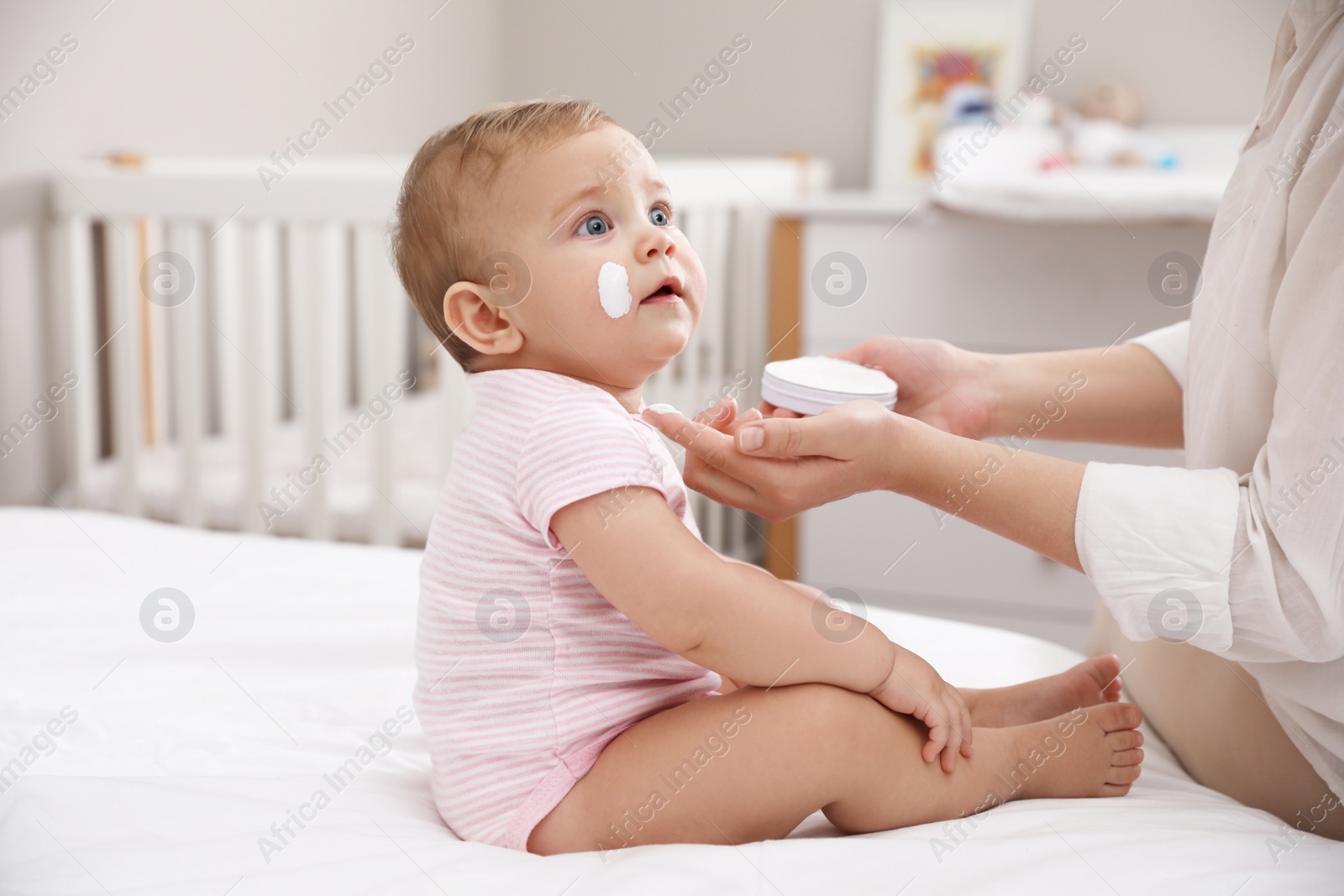 Photo of Mother applying moisturizing cream on her little baby at home, closeup