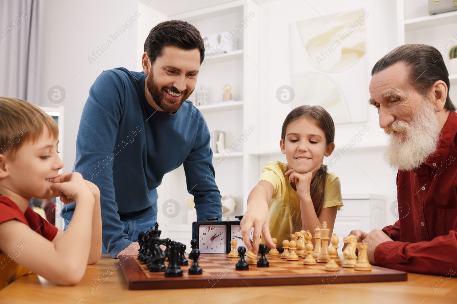 Photo of Family playing chess together at table in room