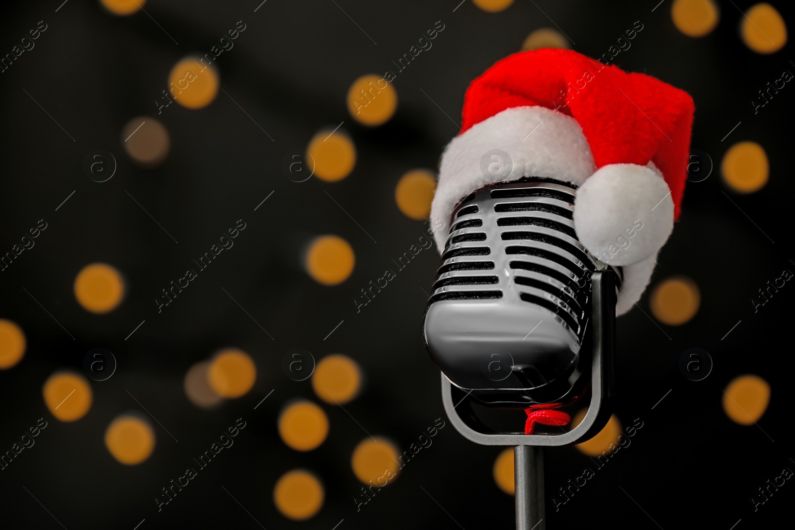 Photo of Retro microphone with Santa hat against blurred lights, space for text. Christmas music