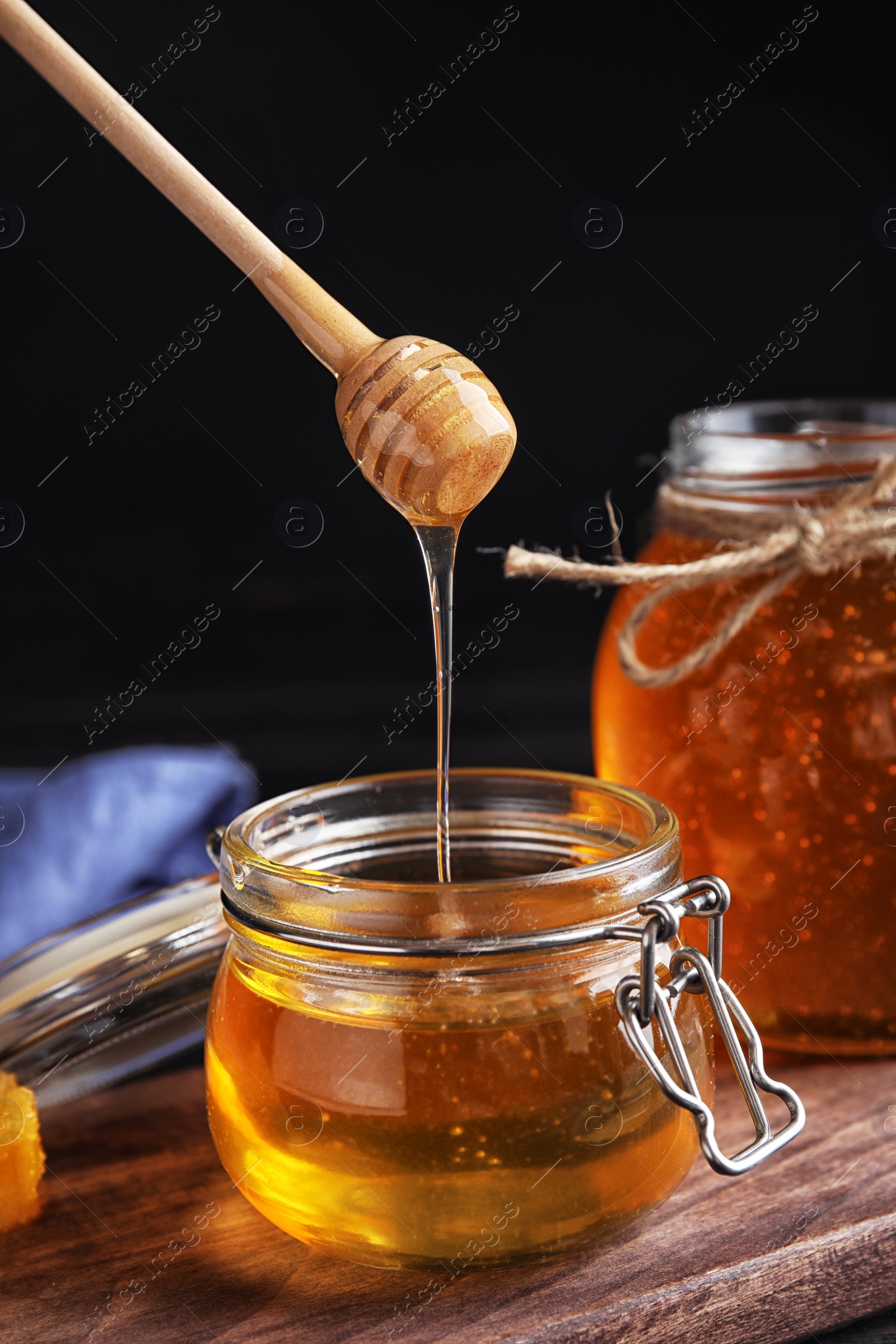 Photo of Honey dripping into jar on wooden board