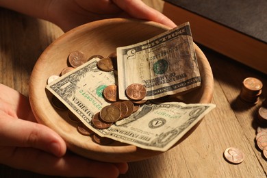 Photo of Donate and give concept. Woman holding bowl with money at wooden table, closeup