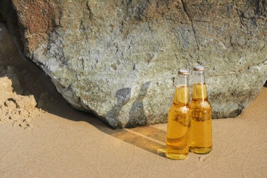 Bottles of cold beer near rock on sandy beach, space for text