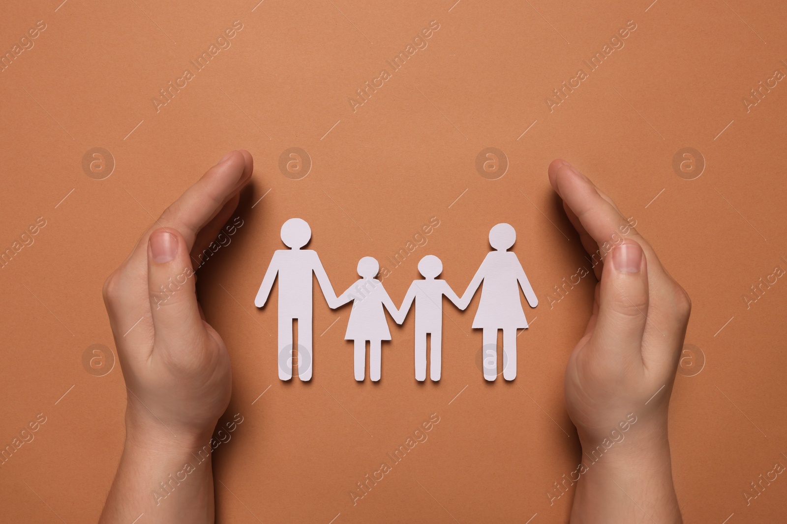Photo of Man protecting paper family figures on brown background, top view. Insurance concept