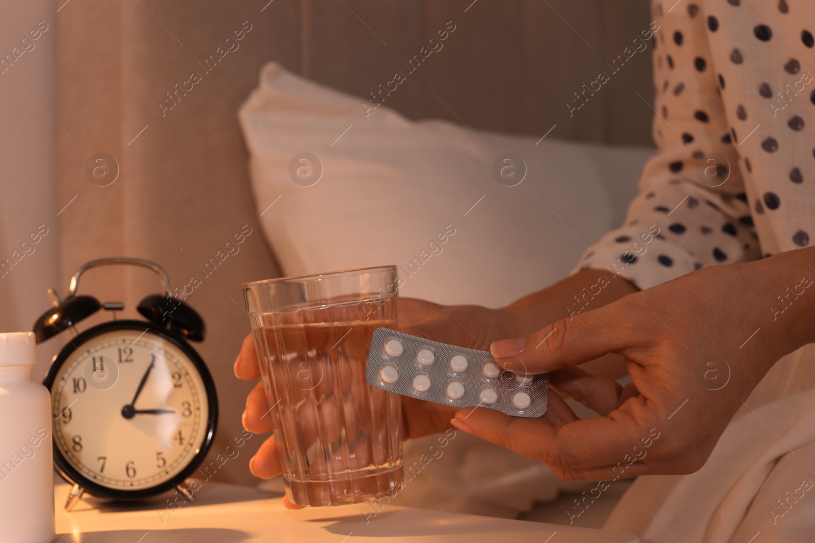 Photo of Woman with glass of water and pills in bedroom at night, closeup. Insomnia concept