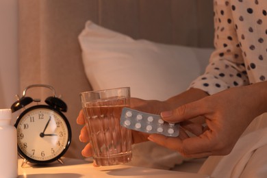 Woman with glass of water and pills in bedroom at night, closeup. Insomnia concept