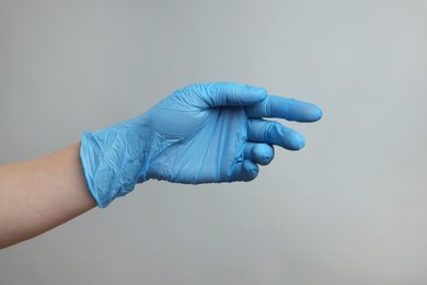 Doctor wearing light blue medical glove on grey background, closeup