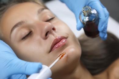 Photo of Cosmetologist applying serum on client's face in salon, closeup