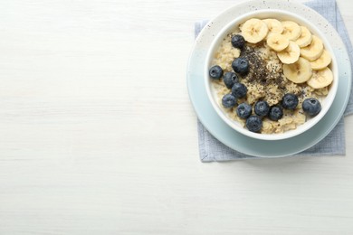 Tasty oatmeal with banana, blueberries and chia seeds served in bowl on white wooden table, top view. Space for text