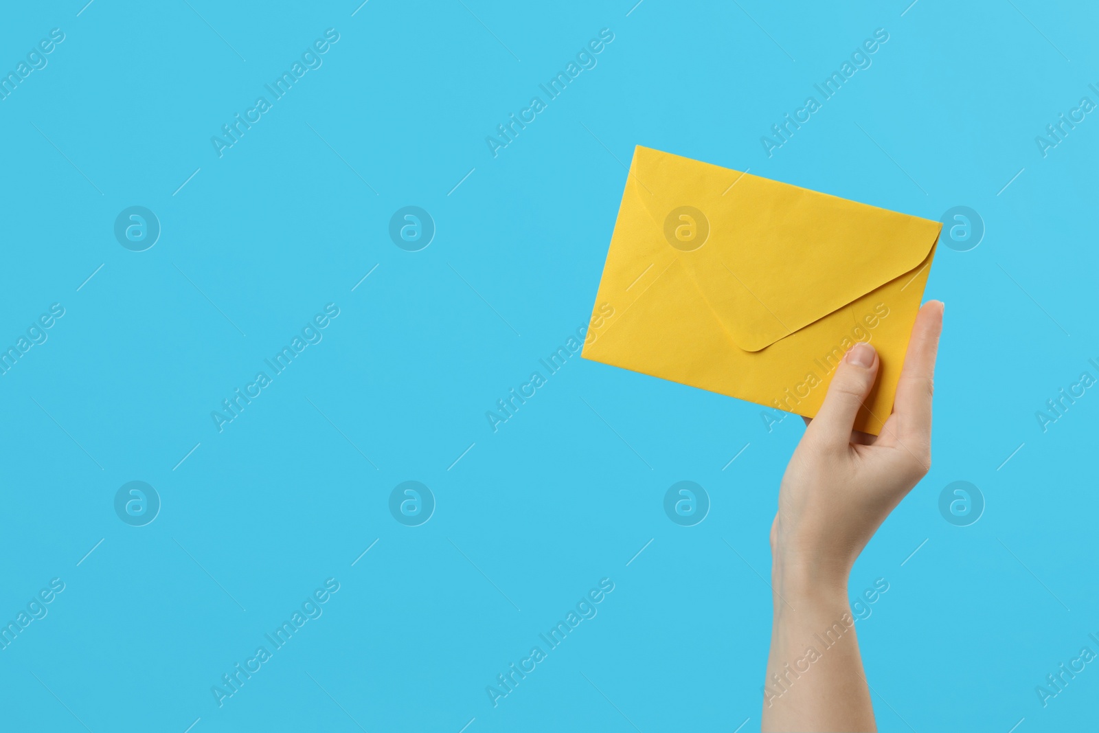 Photo of Woman holding yellow paper envelope on light blue background, closeup. Space for text