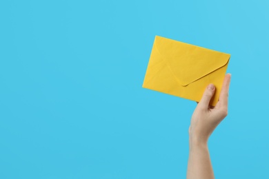 Photo of Woman holding yellow paper envelope on light blue background, closeup. Space for text