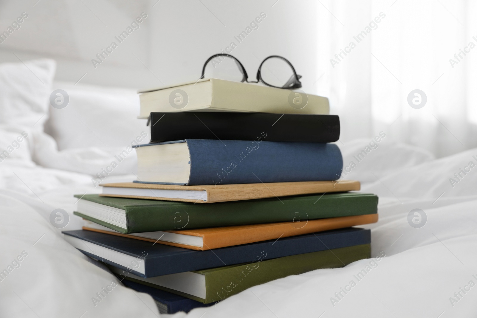 Photo of Hardcover books and glasses on bed indoors