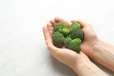 Photo of Young woman holding fresh broccoli over light grey table, closeup. Space for text