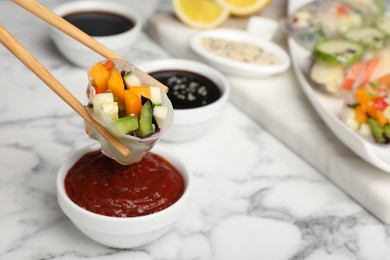 Photo of Dipping delicious roll wrapped in rice paper into sauce at white marble table