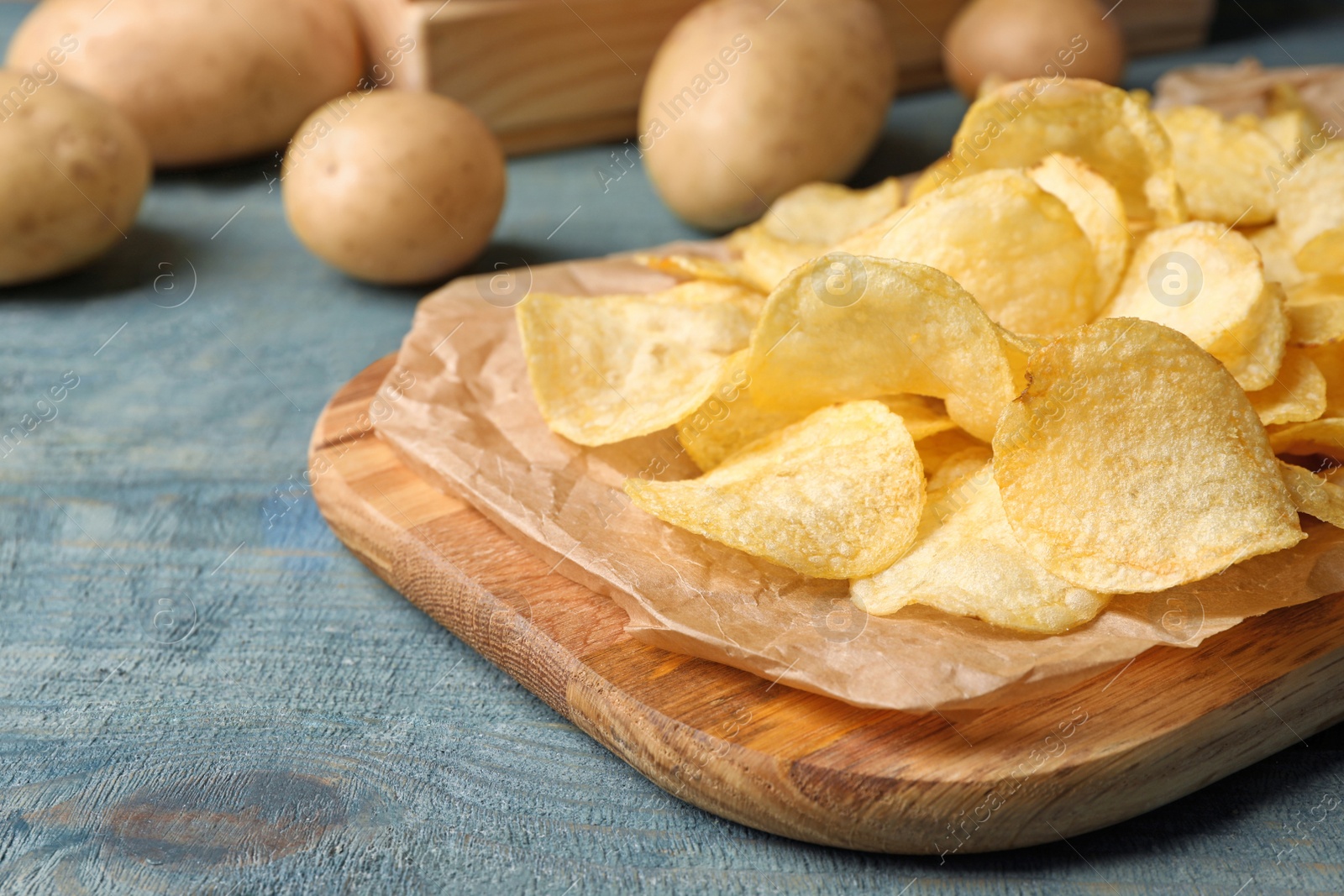 Photo of Board with crispy potato chips on wooden table. Space for text