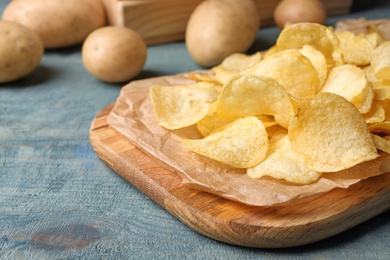 Board with crispy potato chips on wooden table. Space for text