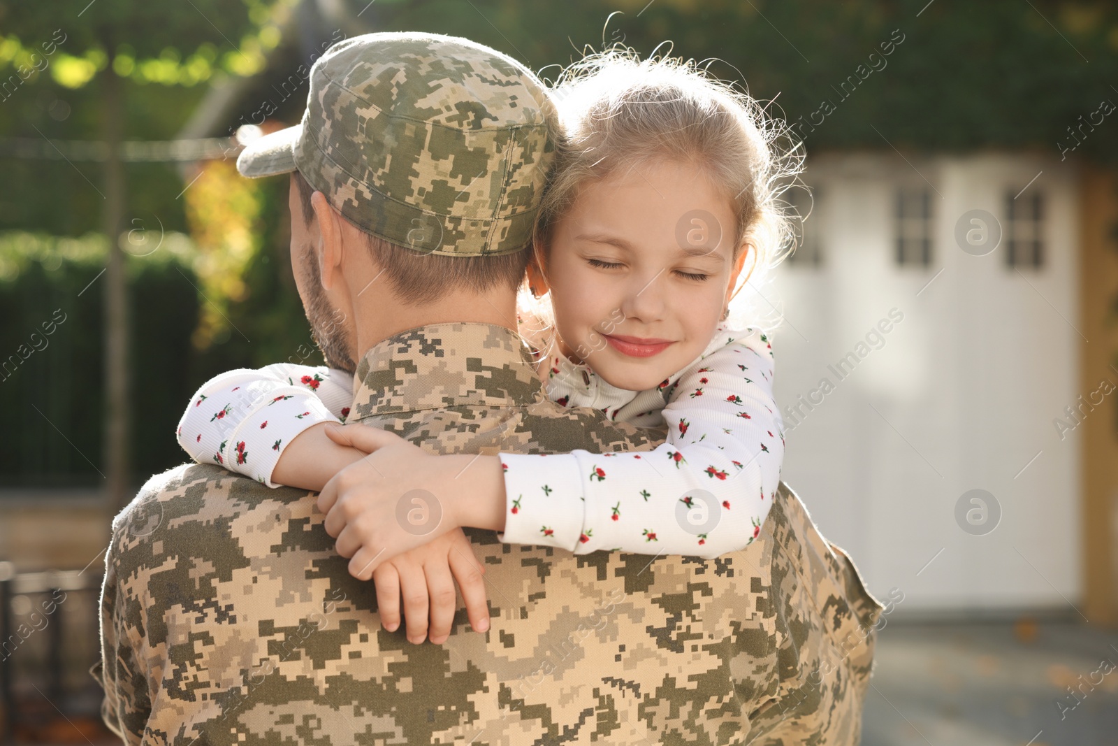 Photo of Soldier in Ukrainian military uniform hugging his daughter outdoors. Family reunion