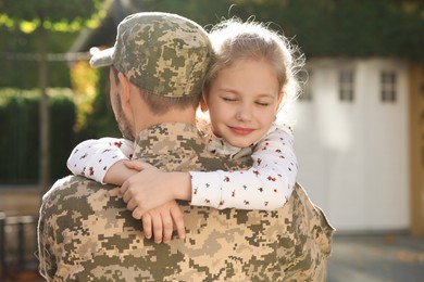 Photo of Soldier in Ukrainian military uniform hugging his daughter outdoors. Family reunion