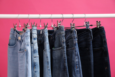 Photo of Rack with stylish jeans on pink background, closeup