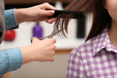 Barber making stylish haircut with professional scissors in beauty salon, closeup